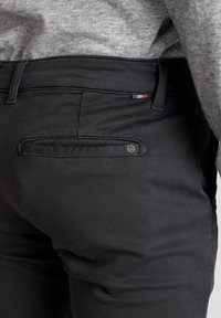Pantaloni neri con tasca posteriore, caratterizzati da un piccolo dettaglio a bandiera colorata e un tessuto strutturato, cuciture a vista e una vestibilità classica.