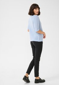 Pull en tricot bleu clair, à manches courtes, porté avec un jean slim noir et des chaussures noires ; présente un motif décoratif et un ourlet arrondi.