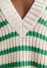 Pull en tricot à col en V, présentant des rayures alternées crème et vertes, avec un motif texturé. Le fil épais lui confère une apparence volumineuse.
