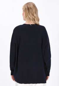 Rento tummansininen neulepusero, jossa on pyöreä kaula-aukko, pitkät hihat ja ribbaatut hihansuut. Pehmeä tekstuuri, minimalistinen muotoilu.