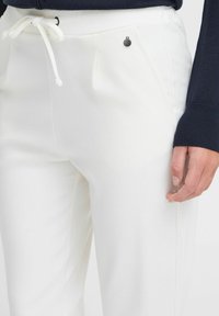 Vita sweatpants med elastisk midjeband, snörning och sidofickor. Har en liten svart knappdetalj nära fickan.