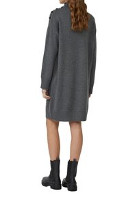 Graues Strickkleid mit Rollkragen und Schulterknöpfen, ausgestattet mit gerippten Bündchen und Saum, kombiniert mit schwarzen Knöchelschuhen.