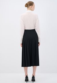 Blusa bianca a maniche lunghe e bottoni abbinata a una gonna midi plissettata nera e scarpe con tacco nere, vista da dietro.