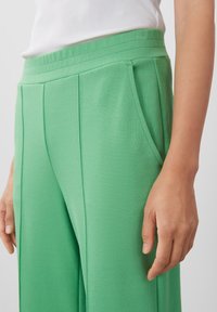 Groene, geribde stoffen broek met een hoge tailleband, voorzien van zakken en gestikte details. De textuur lijkt zacht en gestructureerd.