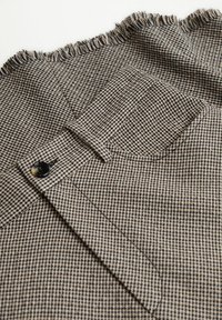 Tissu à motifs marron et noir avec un bord effiloché, une fermeture à bouton et un petit détail de poche. Idéal pour les vêtements sur mesure.