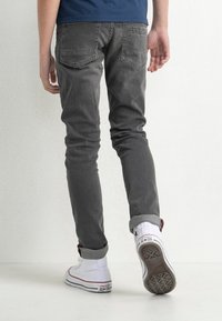 Jeans in denim grigio slim-fit con un leggero effetto lavato, dotati di due tasche posteriori e ricamo del logo discreto, abbinati a sneakers bianche alte.