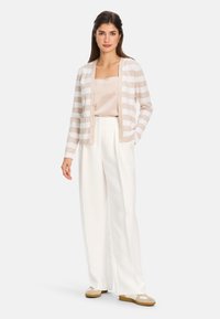 Leichter, beigefarbener gestreifter Cardigan mit Knopfleiste, getragen über einem beigen Top und weißen weit geschnittenen Hosen; weiche Textur, lässiges Design.