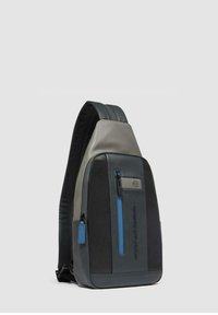 Mochila tipo bandolera en cuero gris y negro, con un bolsillo frontal con cremallera y detalles en azul, y un diseño elegante y en ángulo.