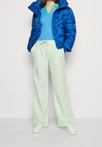 Doudoune bleu vif, pull bleu côtelé avec col vert, pantalon large vert clair et chaussures à plateforme blanches.