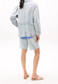 Light blue denim jacket with a relaxed fit, two buttons at the waist, paired with matching denim shorts and light woven slip-on shoes.