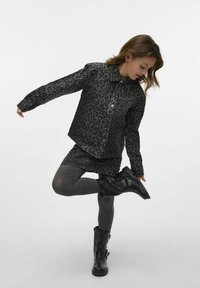 Veste en jean imprimé léopard noir, leggings gris et bottines noires avec embellissements métalliques. La veste possède un col et une fermeture à boutons.