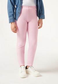 Leggings rosas con una textura suave, cinturilla elástica y costuras cosidas, combinados con zapatillas blancas y una chaqueta de mezclilla.