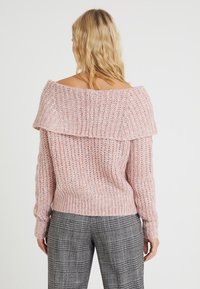 Maglione rosa chiaro lavorato a maglia con design scollato, texture a coste e colletto ripiegato. Indossato con pantaloni grigi a quadri.