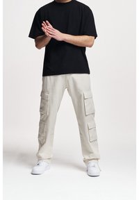 Svart t-shirt med kort ärm i kombination med beige cargobyxor som har flera fickor och vita sneakers, vilket ger en avslappnad och praktisk stil.