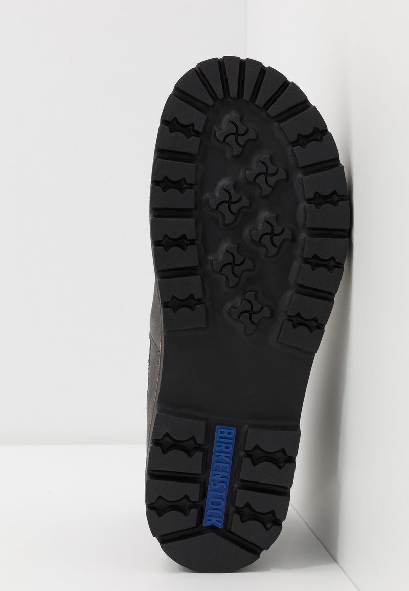 Soletta in gomma nera con modelli di battistrada profondi e logo blu "BIRKENSTOCK". Presenta sezioni rialzate per trazione e stabilità.