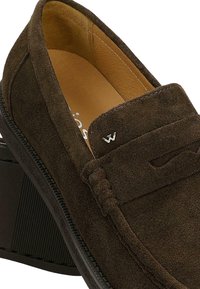 Mocassino in camoscio marrone scuro con tacco basso a blocco e fodera interna in pelle color cuoio, con un piccolo logo metallico a forma di "W" sulla parte frontale.