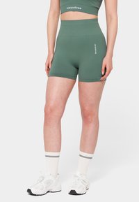 Roheline spordilühike, mis on valmistatud venivast materjalist, kõrge vöökoha, sileda tekstuuri ja väikese logoga esiküljel.