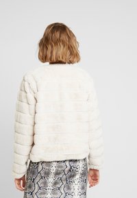 Giacca in pelliccia sintetica color crema con motivo trapuntato, collo rotondo e maniche lunghe, abbinata a una gonna con stampa serpente.