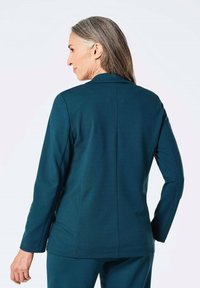 Grove blazer met een getailleerde pasvorm, lange mouwen en een strakke halslijn. Gladde stof met een subtiele glans en rechte rugventilatie.