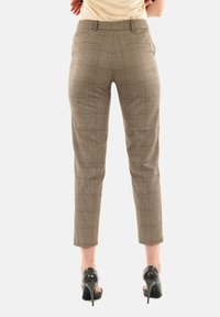 Pantalon à carreaux marron, coupe slim, longueur cheville, avec deux poches arrière. Associé à des chaussures noires à talons hauts.