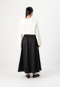 Chunky white knitted sweater with cable pattern, paired with a black ankle-length skirt. Black shoes with circular cutouts.