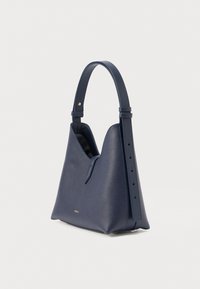 Tumši zila ādas soma ar strukturētu formu, vienu regulējamu siksnu, reljefa detaļu un minimālistisku dizainu bez redzamas metāla daļas.