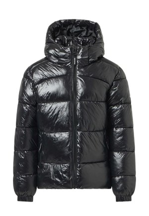 Fille portant une doudoune noire brillante, un jean bleu clair avec de petits points blancs, des bottes noires et un bonnet beige en tricot, debout et regardant sur le côté.