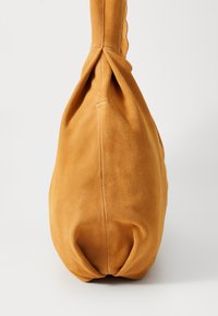 Suede handbag in golden orange, featuring a rounded base and a knotted handle design. Smooth texture with subtle stitching details.