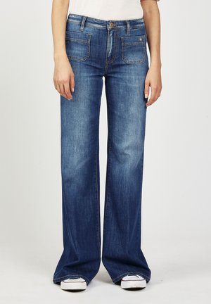 Ausgestellte blaue Jeans aus Denim mit mittelhohem Bund. Sie verfügen über zwei vordere Taschen, zwei hintere Taschen sowie einen sichtbaren Knopf- und Reißverschluss.