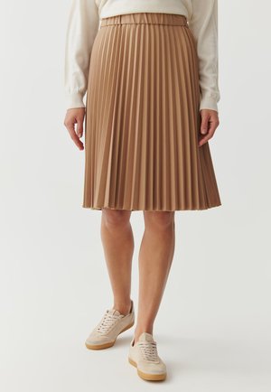 Gonna midi plissettata di colore marrone chiaro con una vita elastica. Tessuto liscio, orlo che finisce a metà polpaccio, abbinata a sneakers beige.