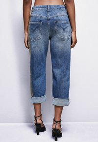 Jeans de mezclilla azul claro con un corte relajado, dobladillos remangados y bolsillos traseros con costuras decorativas. Ligeramente desgastados y con una textura suave.