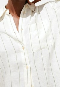 Linned skjorte i off-white med grønne lodrette striber, knaplukning foran, spids krave og en enkelt brystlomme. Blød tekstur og afslappet pasform.