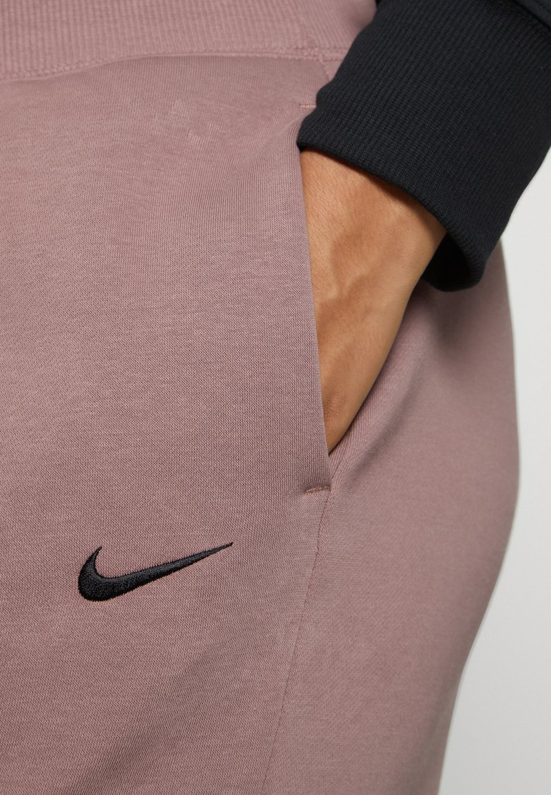 Różowe spodnie sportowe z fakturowanym wykończeniem. Posiadają boczną kieszeń oraz czarne logo Nike wyhaftowane z przodu.