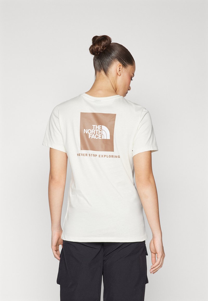 Vit bomullströja med en brun rektangulär logotyp på baksidan med texten "THE NORTH FACE" och "NEVER STOP EXPLORING".