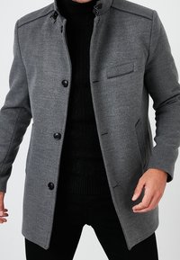 Grijze wollen blend jas met een hoge kraag, voor knopen en een borstzak. Kenmerkt zich door zwarte hardware accenten en een getailleerde pasvorm.