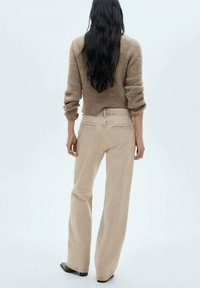Pantalones beige de pierna ancha con cintura alta, que cuentan con bolsillos delanteros y detalles de costura sutiles. Combinados con un suéter de punto marrón.