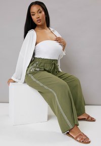 Olivgröna byxor med breda ben och elastisk midja, som har broderade blommor och en sidofläta. Bärs med en vit topp.