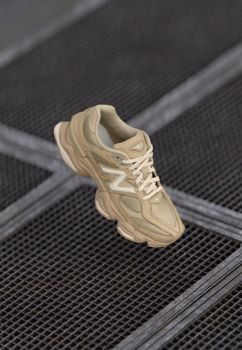 Chaussure de sport beige avec des matériaux en nylon et en daim, dessus texturé, bout arrondi, semelle épaisse et logo bien visible. Lacets de couleur assortie.