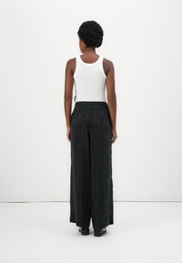 Un débardeur blanc associé à un pantalon large noir à motif floral. Texture lisse, taille élastique et chaussures noires.