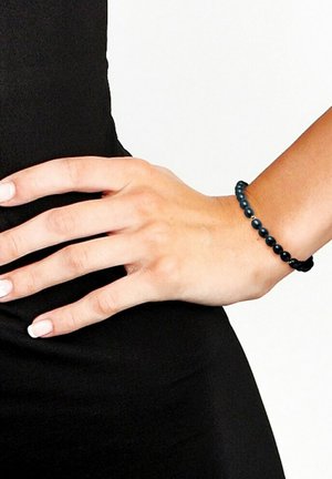 Bracelet en perles noires avec des perles rondes de tailles variées, surface texturée et design extensible, porté sur une main contre un fond noir.