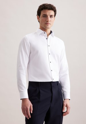 Biała koszula z długim rękawem i zapinanym kołnierzykiem, z ciemnymi guzikami i strukturalnym materiałem, w połączeniu z ciemnymi spodniami. Prosty design.