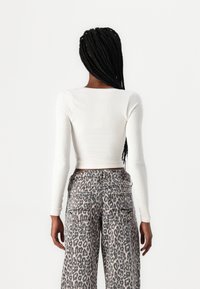 Fehér bordázott, hosszú ujjú crop top magas derekú, leopárdmintás, széles lábú nadrággal párosítva, amely zsebekkel és kontrasztos varrással rendelkezik.