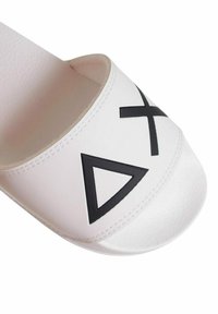 Sandalina bianca in materiale sintetico, con forme geometriche nere—un triangolo e una 'X'—sulla fascia superiore.