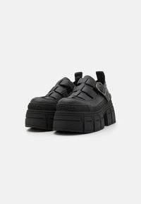 Pantofi cu platformă negri, cu un design din curele împletite, fabricați din material sintetic. Prezintă o talpă texturată și un accent cu cataramă.