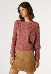 Πλεκτή μπλούζα από υφασμάτινο, σκούρο ροζ υλικό με άνετη εφαρμογή, πλατύ λαιμό και μακριά μανίκια, σε συνδυασμό με μια καφέ κορδούρα φούστα.