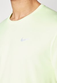 Maglietta atletica a maniche corte in tessuto verde chiaro, con scollatura rotonda e logo Nike riflettente in argento sul lato sinistro del petto.