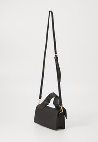 Bolso de mano de cuero negro con dos asas; una ajustable y larga, la otra corta y estructurada. Acentos de hardware dorado y textura suave.