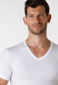T-shirt bianco a maniche corte con scollatura a V, realizzato in tessuto morbido, presenta una vestibilità aderente e un dettaglio a contrasto sul colletto.