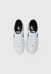 Sneakers brancos da Nike Air com detalhes em preto, apresentando um cabedal de couro liso, caixa do dedão perfurada, atacadores planos e colarinho almofadado.