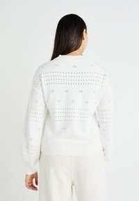 Pulover alb tricotat cu design din dantelă, având o croială lejeră, margine ribbată și mâneci tip balon, prezentat din spate.